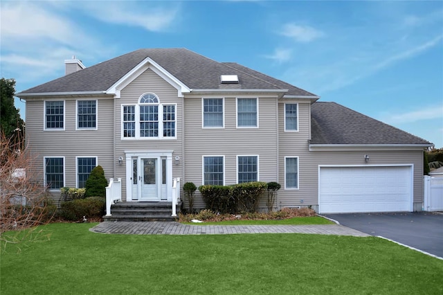 colonial-style house featuring driveway, a front lawn, roof with shingles, and an attached garage