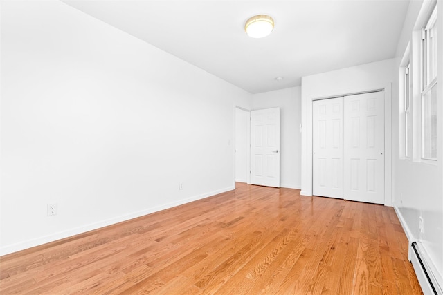 unfurnished bedroom with light wood-style floors, a closet, baseboards, and baseboard heating