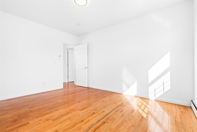 empty room featuring baseboard heating, light wood-style flooring, and baseboards