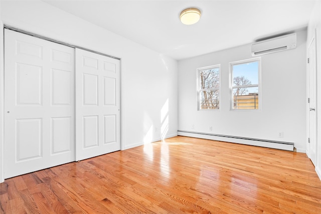 unfurnished bedroom with a closet, a wall mounted AC, a baseboard heating unit, wood finished floors, and baseboards