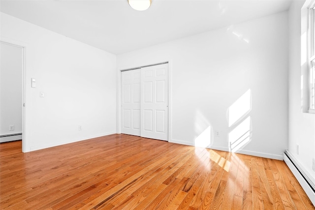 unfurnished bedroom featuring light wood-style floors, baseboards, baseboard heating, and a closet