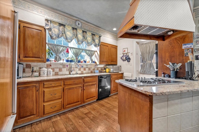 kitchen with brown cabinetry, premium range hood, stainless steel appliances, and a sink