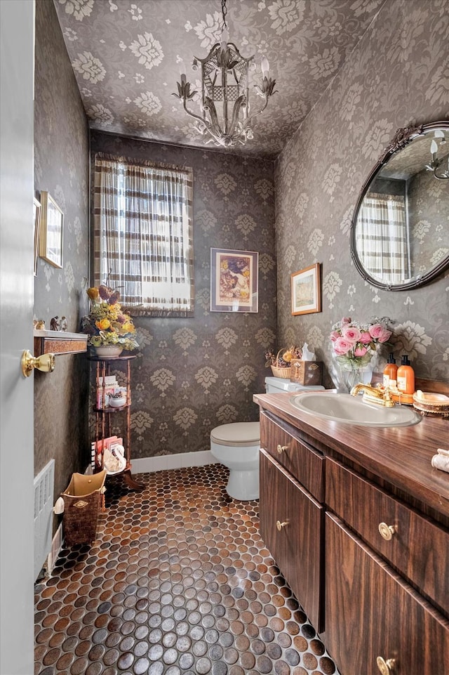 bathroom featuring toilet, vanity, baseboards, and wallpapered walls