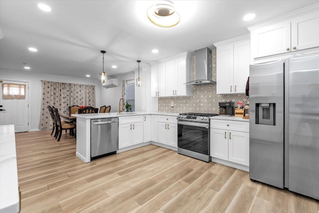 kitchen featuring light wood finished floors, a wall mounted air conditioner, light countertops, stainless steel appliances, and wall chimney range hood