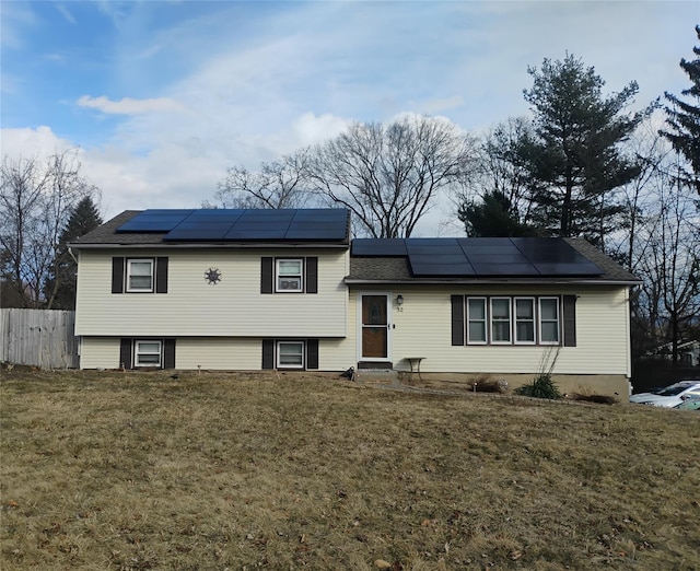 tri-level home with solar panels, a front lawn, and fence