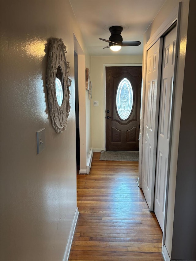 doorway featuring baseboards, wood finished floors, and a ceiling fan