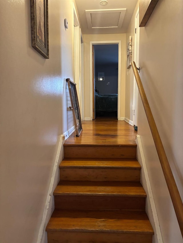 stairs featuring attic access, wood finished floors, and baseboards