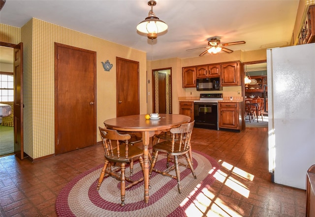 dining room with brick floor, a ceiling fan, and wallpapered walls