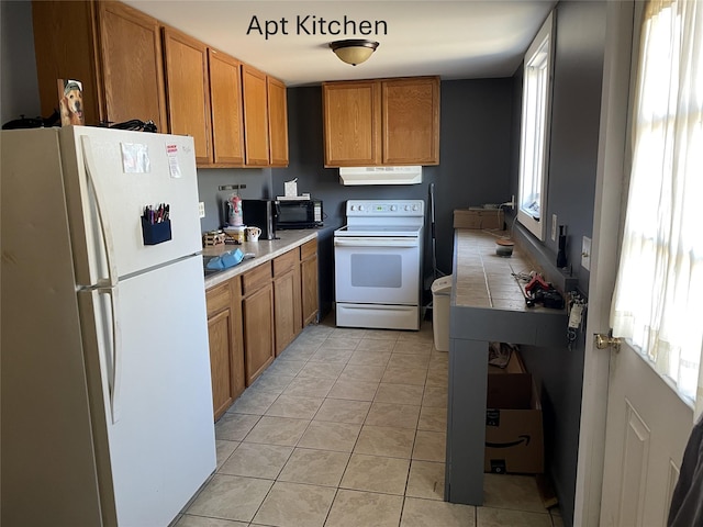 kitchen with white appliances, light tile patterned floors, brown cabinetry, light countertops, and exhaust hood