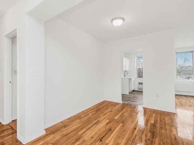 empty room featuring radiator, baseboards, a sink, and light wood finished floors