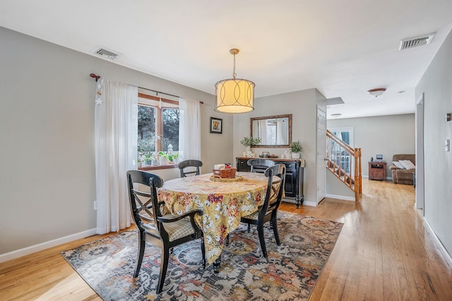 dining room featuring light wood finished floors, baseboards, visible vents, and stairway