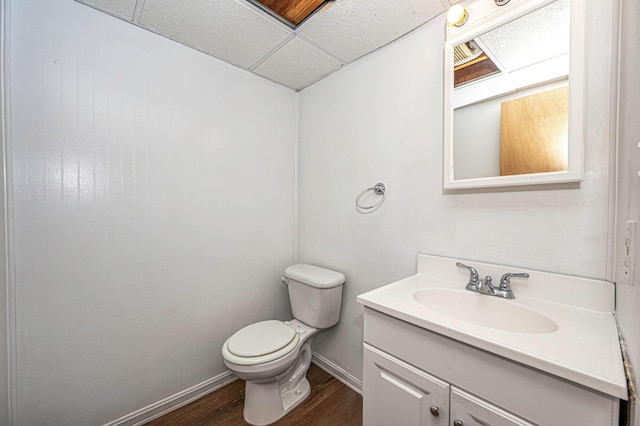 bathroom featuring a drop ceiling, toilet, wood finished floors, vanity, and baseboards