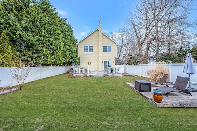 rear view of property featuring a fenced backyard, a chimney, a deck, and a lawn