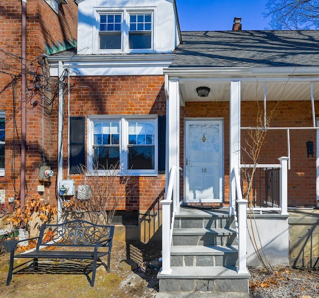 doorway to property featuring a shingled roof and brick siding