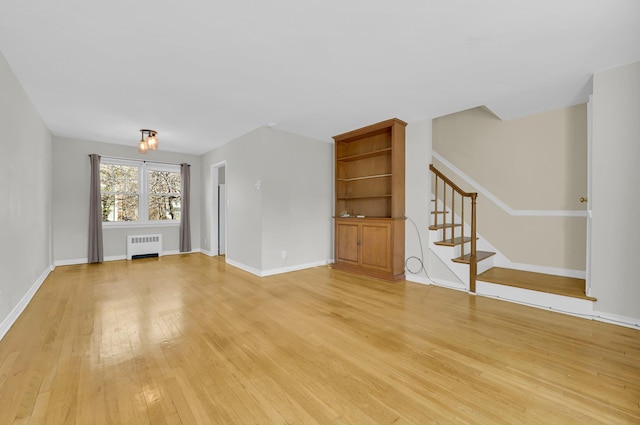 unfurnished living room with radiator, light wood-style floors, baseboards, and stairway