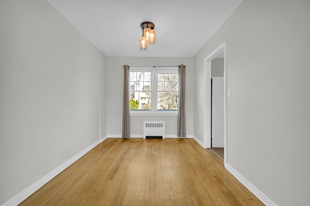 unfurnished room featuring baseboards, light wood finished floors, and radiator heating unit