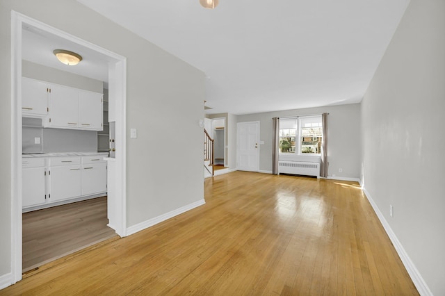 unfurnished living room with light wood-type flooring, radiator heating unit, stairs, and baseboards