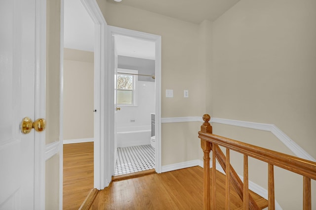 corridor with light wood finished floors, an upstairs landing, and baseboards