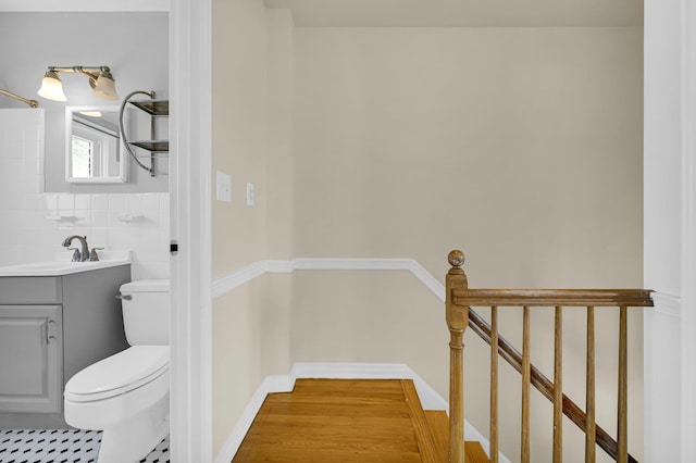 bathroom with toilet, wood finished floors, vanity, baseboards, and tile walls