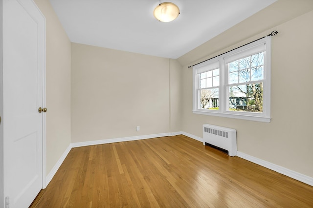 empty room featuring radiator, baseboards, and light wood finished floors