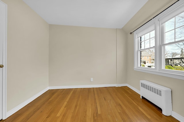 spare room with radiator, light wood finished floors, and baseboards