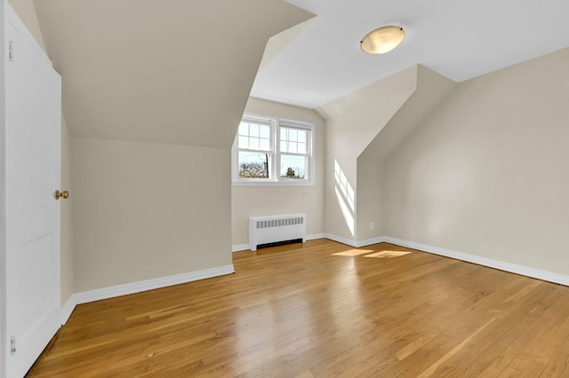 bonus room with radiator, light wood-style flooring, baseboards, and vaulted ceiling