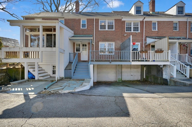 exterior space with brick siding, a chimney, an attached garage, driveway, and stairs