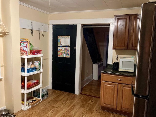 kitchen featuring dark countertops, white microwave, wood finished floors, freestanding refrigerator, and crown molding