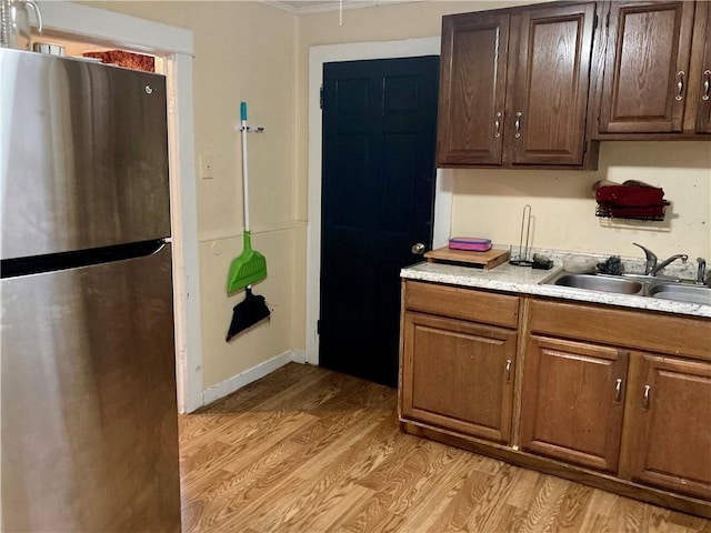 kitchen featuring baseboards, light wood-style flooring, freestanding refrigerator, light countertops, and a sink