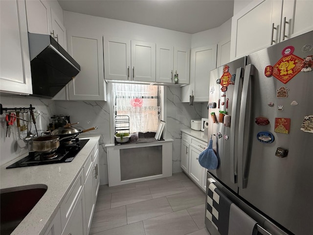 kitchen featuring tasteful backsplash, ventilation hood, a sink, and freestanding refrigerator