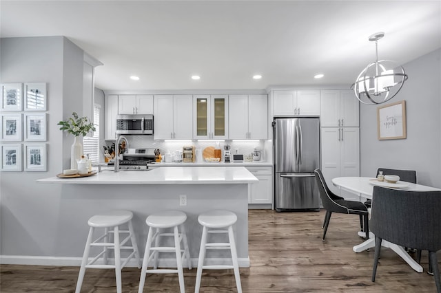 kitchen featuring glass insert cabinets, appliances with stainless steel finishes, dark wood-style flooring, a kitchen bar, and white cabinetry