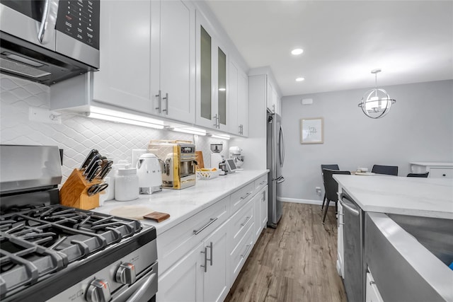 kitchen with stainless steel appliances, wood finished floors, white cabinets, backsplash, and glass insert cabinets