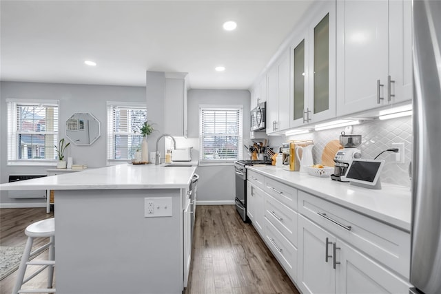kitchen with backsplash, appliances with stainless steel finishes, white cabinetry, a sink, and a kitchen breakfast bar