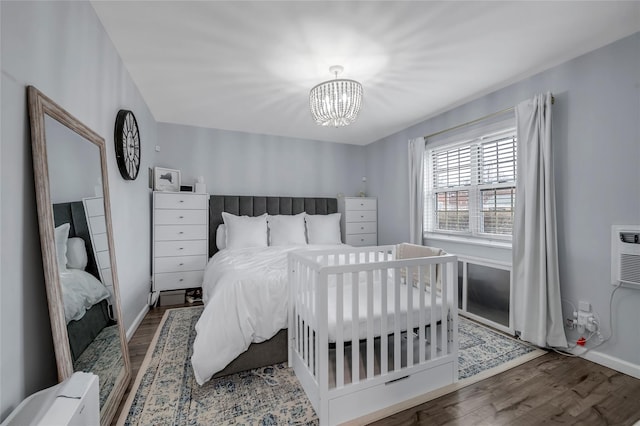 bedroom with a chandelier, a wall unit AC, wood finished floors, and baseboards