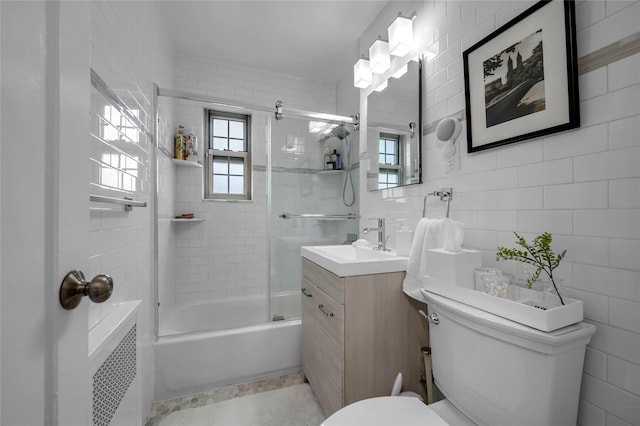 full bathroom with toilet, vanity, tile walls, combined bath / shower with glass door, and radiator