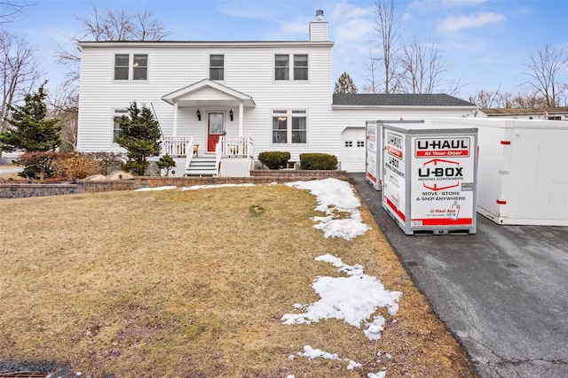 view of front of home featuring a front lawn, driveway, a chimney, and an attached garage