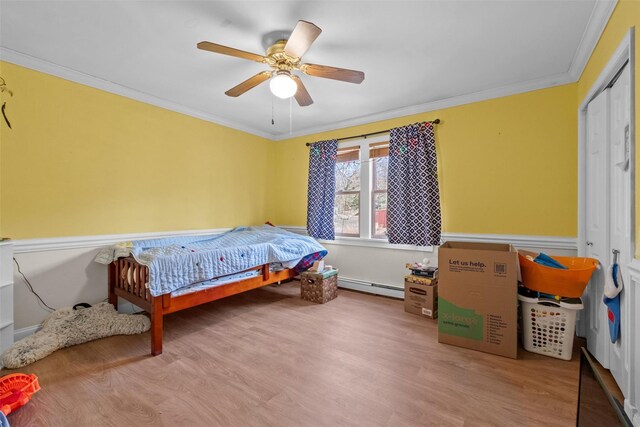 bedroom with a baseboard heating unit, ceiling fan, wood finished floors, and crown molding