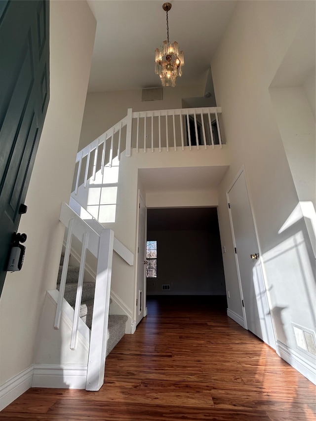 stairway with visible vents, a high ceiling, an inviting chandelier, wood finished floors, and baseboards