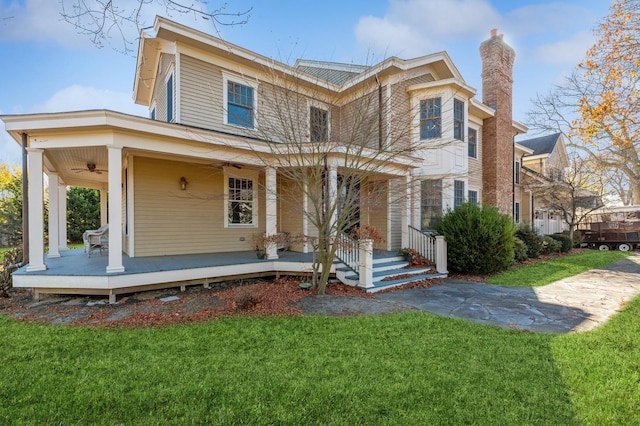 view of front of property featuring covered porch, a chimney, a front yard, and a ceiling fan