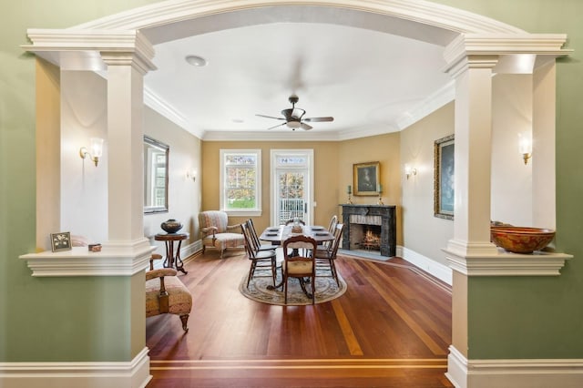 dining space featuring hardwood / wood-style floors, a high end fireplace, decorative columns, and a ceiling fan