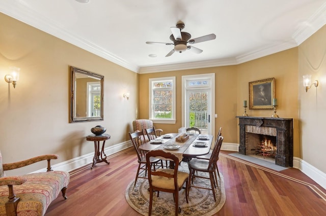 dining space with a premium fireplace, baseboards, wood finished floors, and ornamental molding