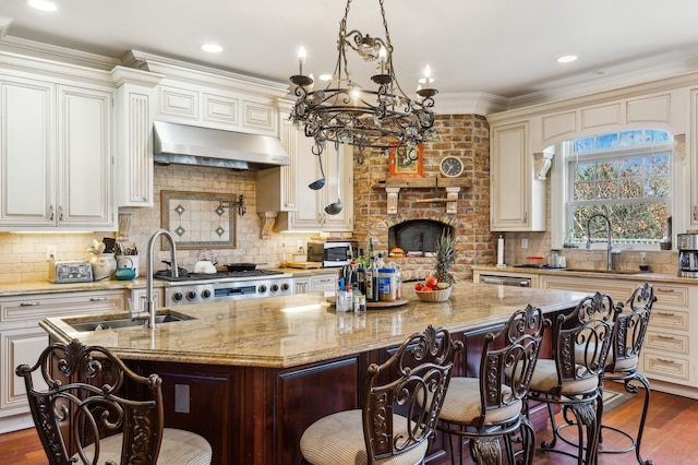 kitchen featuring light stone countertops, a center island with sink, extractor fan, and a sink