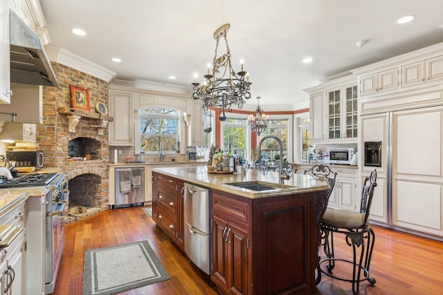 kitchen with high end appliances, crown molding, under cabinet range hood, a kitchen bar, and a sink