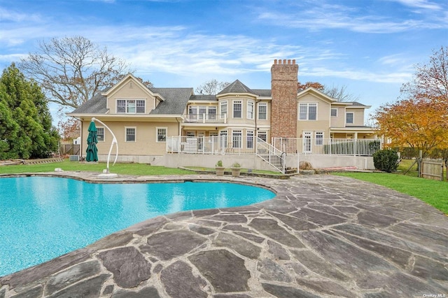 back of property with a balcony, fence, a fenced in pool, and a yard