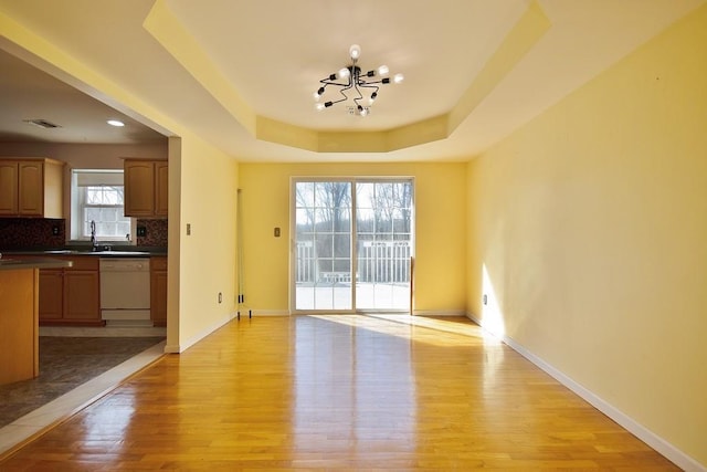 interior space with light wood-style flooring, a raised ceiling, baseboards, and a sink