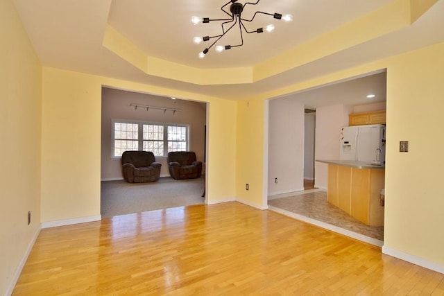 spare room featuring baseboards, light wood-style floors, and a tray ceiling