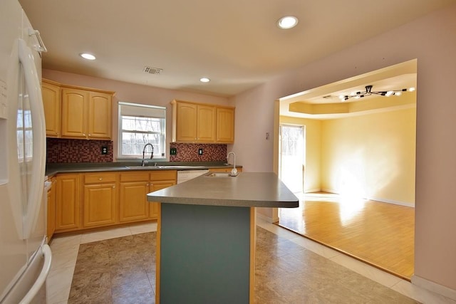 kitchen with light brown cabinetry, visible vents, freestanding refrigerator, and a sink