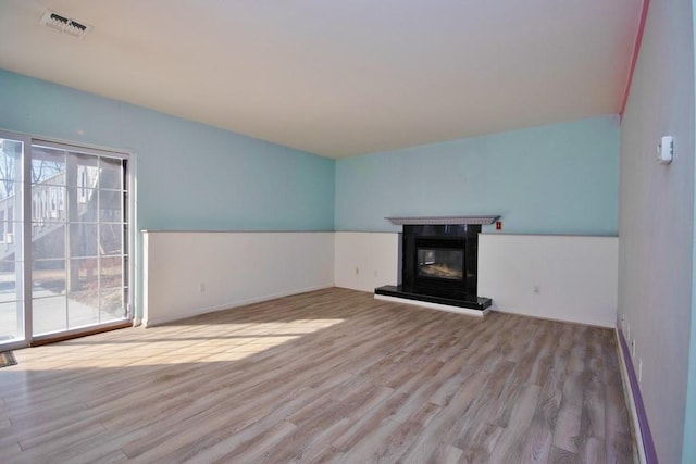 unfurnished living room featuring visible vents, wood finished floors, and a glass covered fireplace