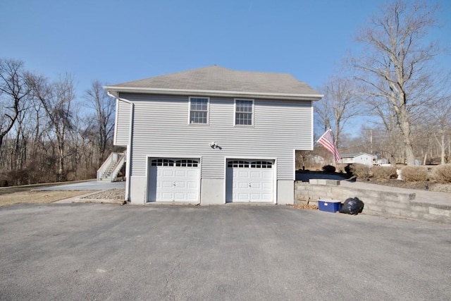 view of side of home featuring aphalt driveway, an attached garage, and stairway