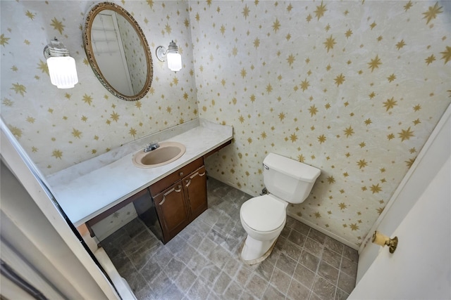 bathroom with vanity, toilet, and wallpapered walls